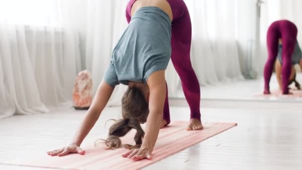 woman does downward-facing dog pose at yoga studio - Materiał filmowy, wideo