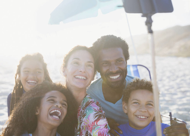 Famiglia multietnica felice e giocosa che si fa selfie con bastone selfie sulla soleggiata spiaggia estiva
 - Foto, immagini