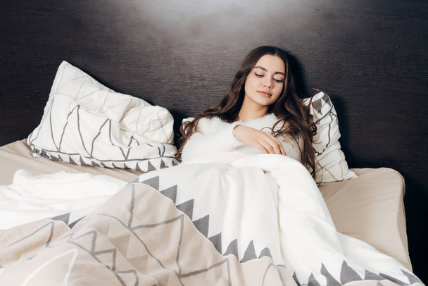 cute long-haired girl sleeping in bed under a white blanket, tired - Fotó, kép