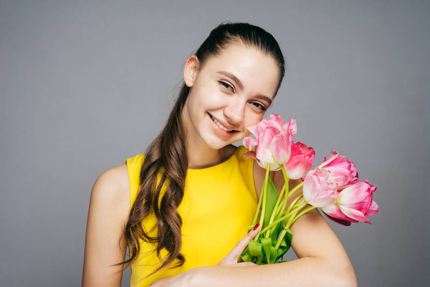 joyful young girl in yellow dress celebrates, holds bouquet of flowers and smiles - Zdjęcie, obraz