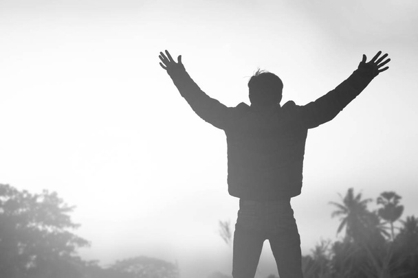 Emotional wellness concept: Silhouette of man raised hands at sunset meadow background - Photo, Image