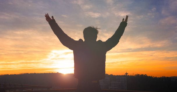 Emotional wellness concept: Silhouette of man raised hands at sunset meadow background - Photo, Image