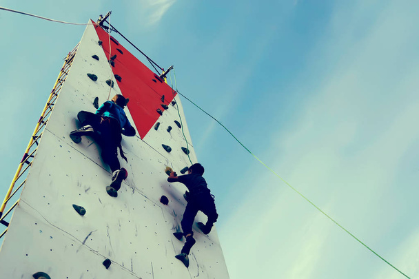 Homem subindo uma parede em um exercício para montanhismo no auge de. A parede de escalada contra um céu azul
 - Foto, Imagem