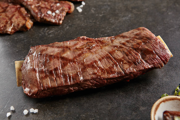 Hot Grilled Whole Flank Steak on Black Stone Background. Fresh Juicy Medium Rare Beef Grillsteak. Barbecue Meat Close Up - Photo, image