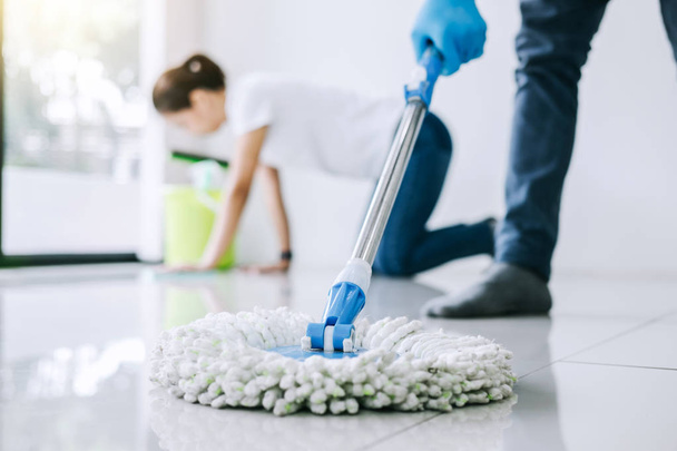 Housekeeping and cleaning concept, Young couple in blue rubber gloves wiping dust using mop and duster while helping cleaning on floor at home. - Photo, image