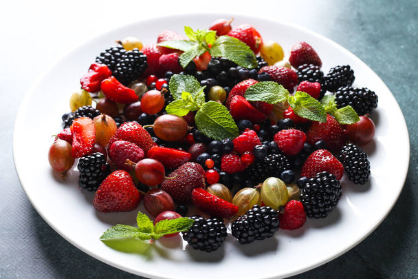 Φρουτοσαλάτα με βατόμουρο, σταφίδα, φράουλα, μούρα, φραγκοστάφυλα, βατόμουρα και μέντας σε ένα άσπρο πιάτο. - Φωτογραφία, εικόνα