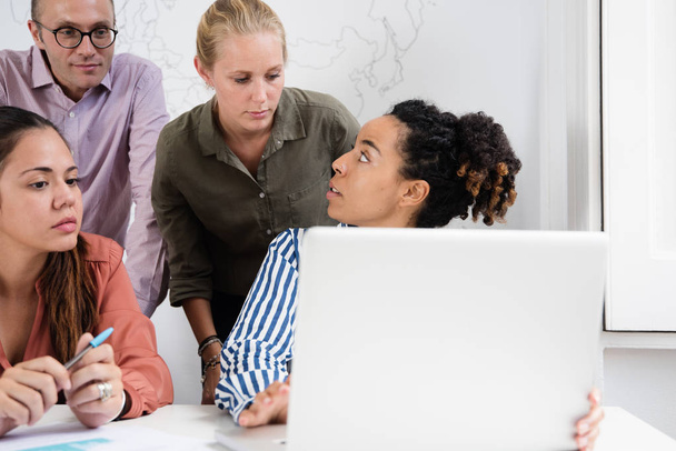 Business team gathered around a laptop in an office discussing something that they are all looking at and gesturing towards the screen - Photo, Image