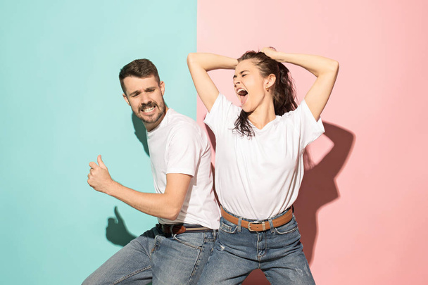 A couple of young funny and happy man and woman dancing hip-hop at studio on blue and pink trendy color background. Human emotions, youth, love and lifestyle concept - Photo, image