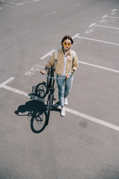 vista de ángulo alto de la mujer con estilo con bicicleta en el estacionamiento
  - Foto, Imagen