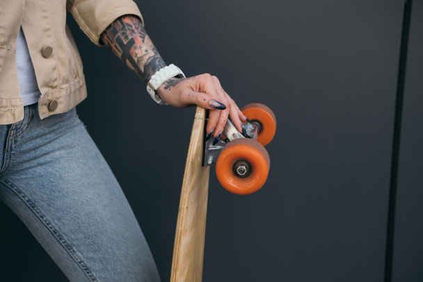 cropped image of tattooed woman holding skateboard near black wall - 写真・画像