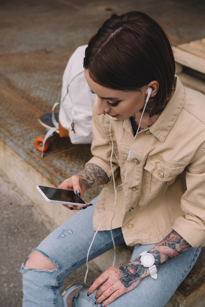 high angle view of stylish tattooed woman in earphones listening music with smartphone  - Photo, Image