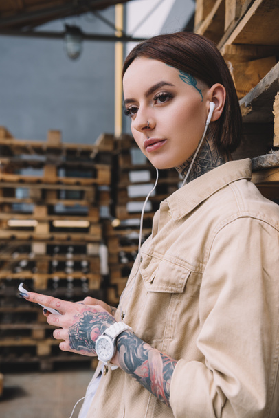 young tattooed woman in earphones listening music with smartphone - Photo, image