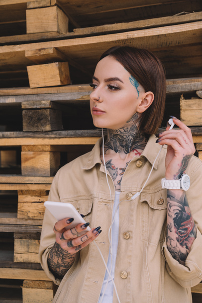atractiva mujer tatuada en auriculares escuchando música con teléfono inteligente
  - Foto, Imagen