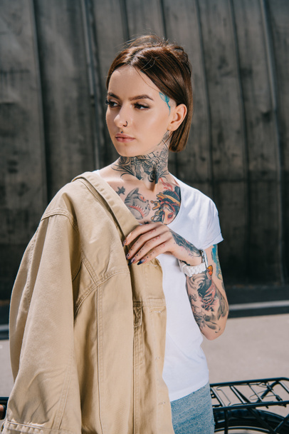 portrait of tattooed woman with jacket on shoulder looking away - Foto, Imagem