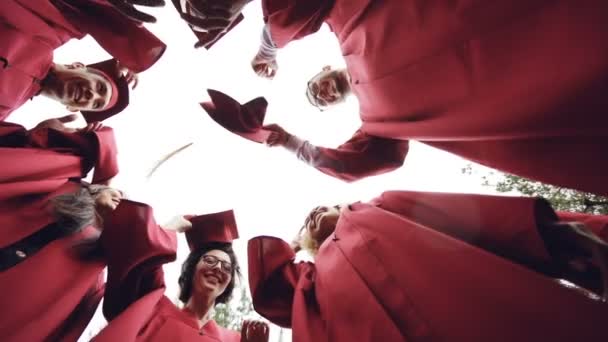 Plan à angle bas de filles et de gars diplômés jetant des mortiers dans le ciel et riant. Célébration de la remise des diplômes, vêtements traditionnels et concept éducatif
. - Séquence, vidéo