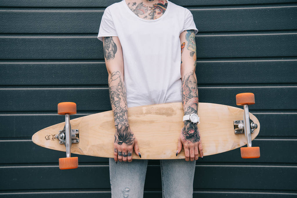 ořízne obraz žena s tetováním držení skateboardu černé zdi  - Fotografie, Obrázek