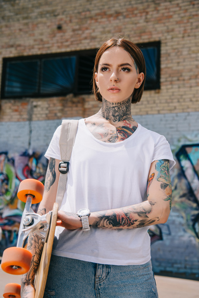 joven atractivo tatuado chica sosteniendo monopatín en la calle
 - Foto, Imagen