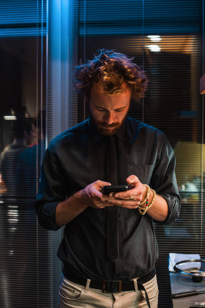 Portrait de jeune homme aux cheveux bouclés utilisant smartphone intérieur
 - Photo, image