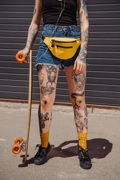 cropped image of stylish tattooed woman standing with skateboard at street - Valokuva, kuva
