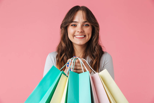 Photo of happy young pretty woman shopaholic standing isolated over pink wall background looking camera holding shopping bags. - Fotoğraf, Görsel