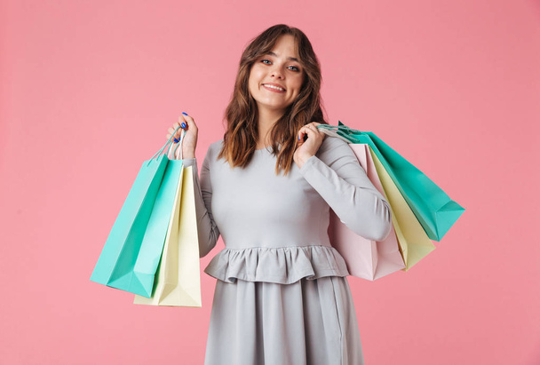 Photo of happy young pretty woman shopaholic standing isolated over pink wall background looking camera holding shopping bags. - Zdjęcie, obraz