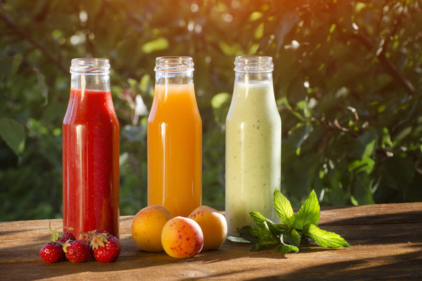 Bottles with juice and fruits on a green background, food concept. Summer, sunlight - Photo, Image