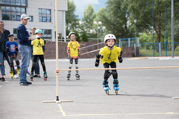 Belarús, Gomel, 24 de junio de 2018. Central Park. Competición de los niños en el deporte del rodillo. Una muchacha en patines saltando sobre un palillo de deportes
 - Foto, Imagen