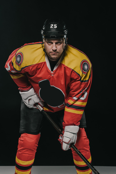 jugador de hockey sobre hielo profesional sosteniendo palo de hockey y mirando a la cámara en negro
  - Foto, Imagen