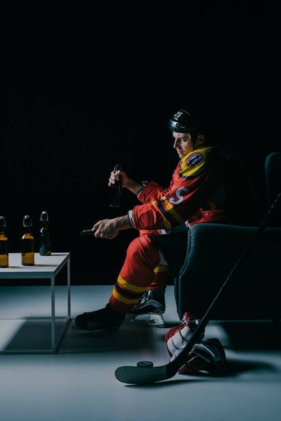 side view of hockey player drinking beer and watching tv on black  - Fotografie, Obrázek