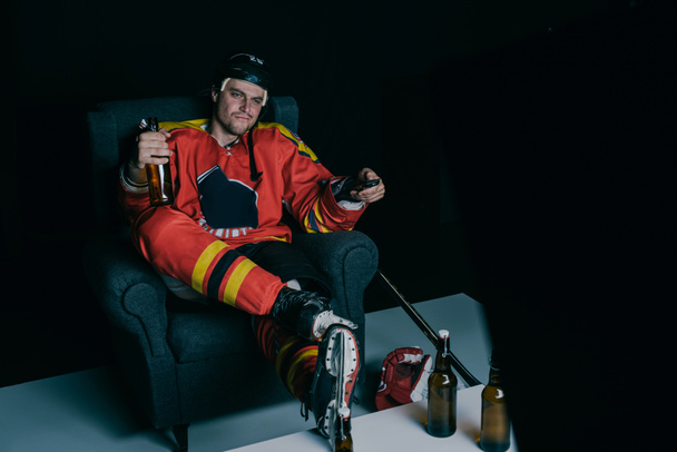 Eishockeyspieler trinkt Bier und schaut Fernsehen auf schwarz   - Foto, Bild