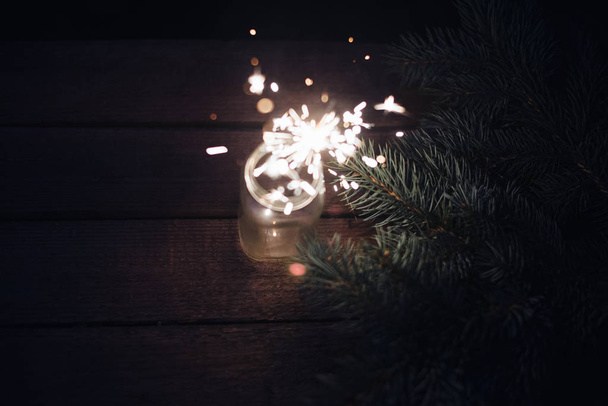 Bengal light in a glass jar on a wooden background with branches of a Christmas tree - Fotografie, Obrázek