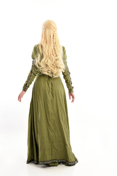 full length portrait of blonde girl wearing green medieval gown. standing pose facing away from the camera, isolated on white studio background. - Photo, Image
