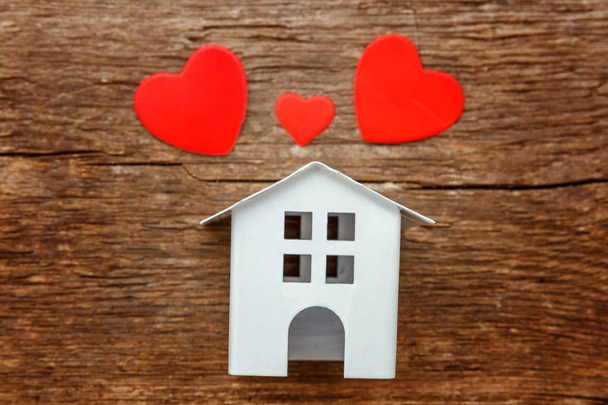 Miniatuur wit speelgoed huis met drie rode harten op een rustieke oude vintage houten achtergrond. Hypotheek eigendom verzekering droom huis concept - Foto, afbeelding