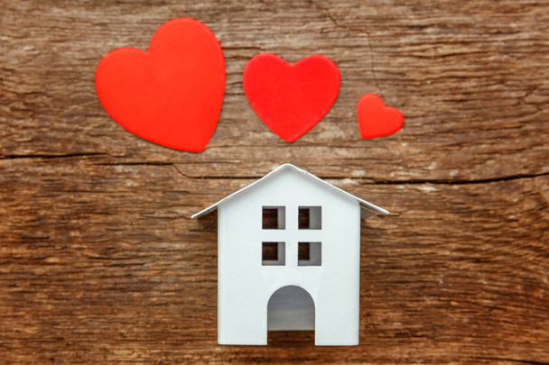 Casa miniatura de juguete blanco con corazones rojos sobre un rústico fondo de madera vintage antiguo. Hipoteca propiedad seguro sueño casa concepto
 - Foto, imagen