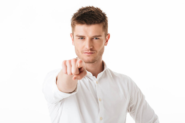 Portrait of a confident young man pointing finger at camera isolated over white background - Foto, Imagen