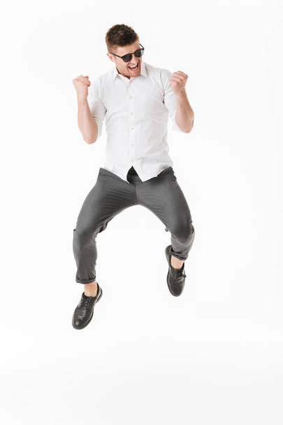 Full length portrait of a happy young man in sunglasses jumping isolated over white background - Photo, Image