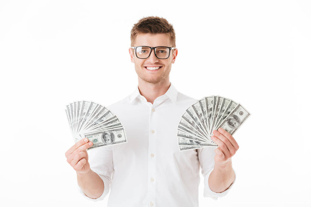Portret szczęśliwy młody człowiek w okularach trzyma banknoty pieniądze na białym tle nad białym tle - Zdjęcie, obraz