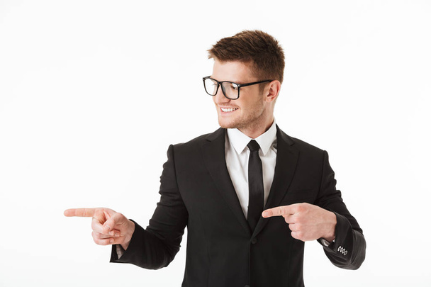 Portrait of a happy young businessman in suit and eyewear pointing fingers away at copy space isolated over white background - Foto, Imagem