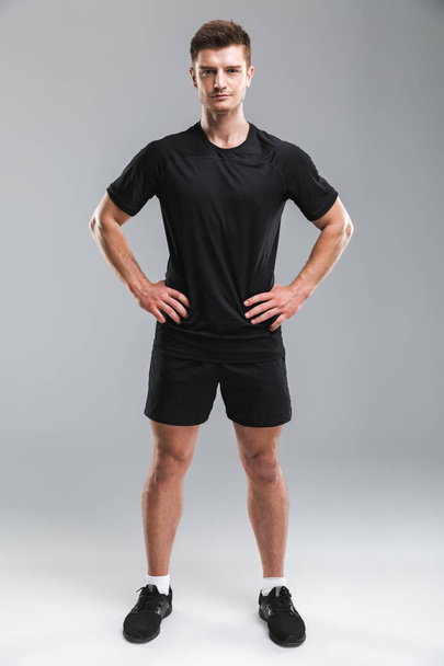 Full length portrait of a focused young sportsman standing with arms on hips isolated over gray background - Photo, Image