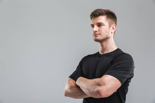Portrait of a confident young sportsman standing with arms folded isolated over gray background - Foto, Imagen