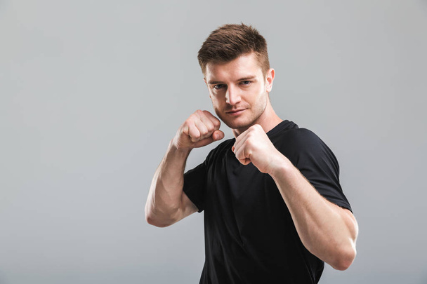Portrait of a focused young sportsman standing ready to fight isolated over gray background - Фото, зображення