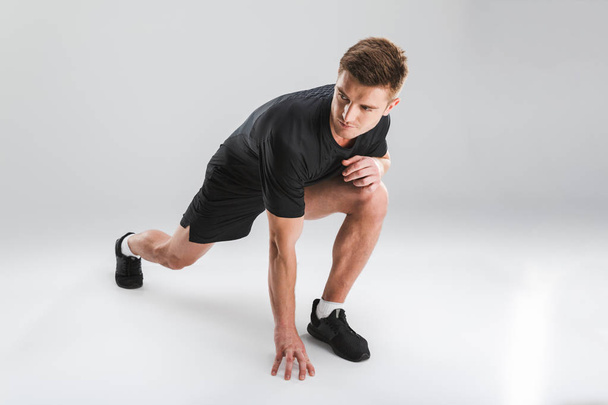 Portrait of a motivated young sportsman doing stretching exercises isolated over gray background - Photo, image