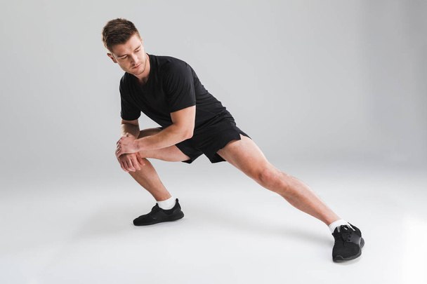 Portrait of a fit young sportsman doing stretching exercises isolated over gray background - Foto, Imagem