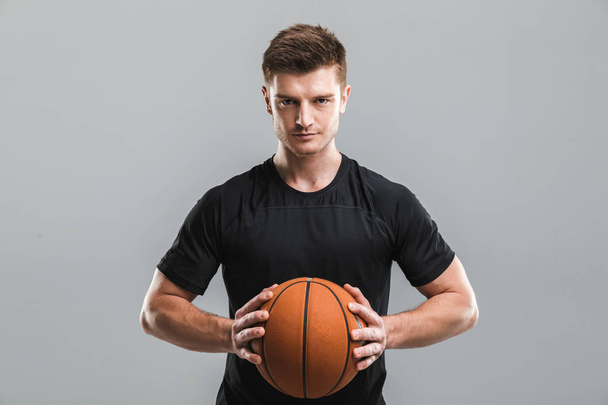 Portrait of a motivated young sportsman holding basketball isolated over gray background - Φωτογραφία, εικόνα