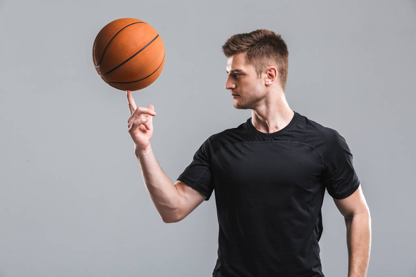 Portrait of a young sportsman playing basketball isolated over gray background - Foto, Imagen