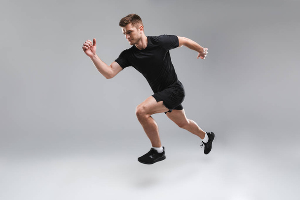 Full length portrait of a concentrated young sportsman running fast isolated over gray background - Фото, изображение
