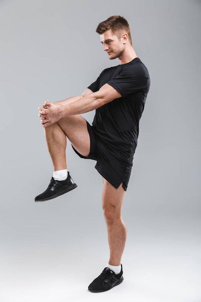 Portrait of a focused young sportsman doing stretching exercises isolated over gray background - Photo, Image