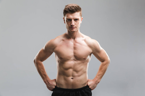 Portrait of a focused shirtless sportsman standing with arms on hips isolated over gray background - Foto, Bild
