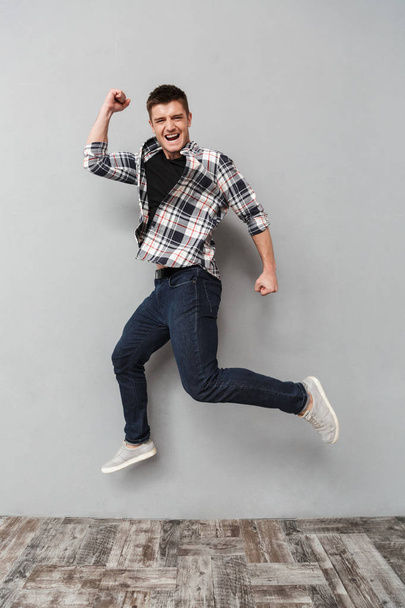 Full length portrait of a happy young man jumping over gray background - Photo, Image