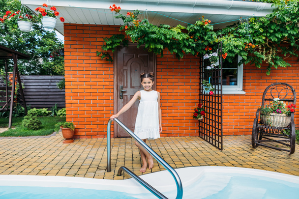 adorable little child standing at swimming pool near country house - Photo, Image
